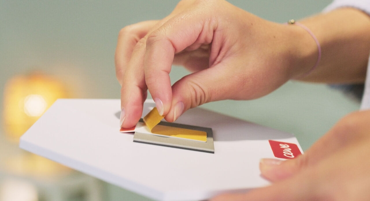 A hand places a yellow label on a CEWE greeting card.