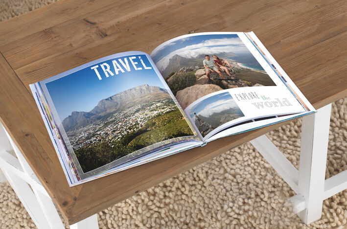 An open CEWE photo book with travel pictures on a wooden table.