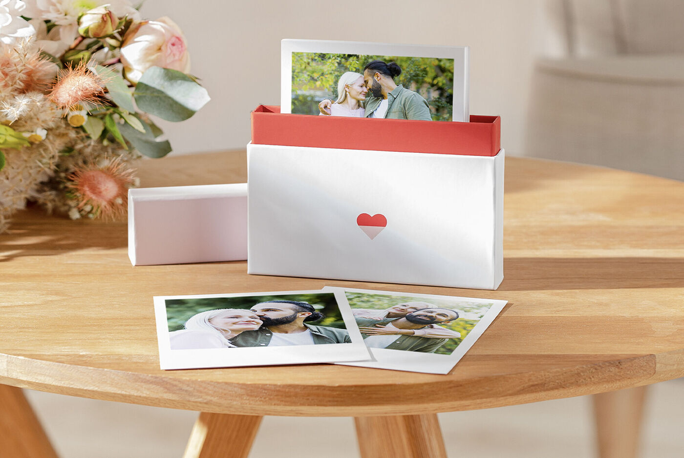 A lovingly designed box with photos that holds memories. The box has a red inner edge and a heart symbol. Three photos lie on the front, two show a couple.
