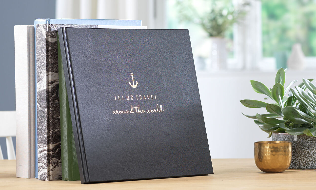 Black photo book titled 'Let Us Travel around the World' on a table.